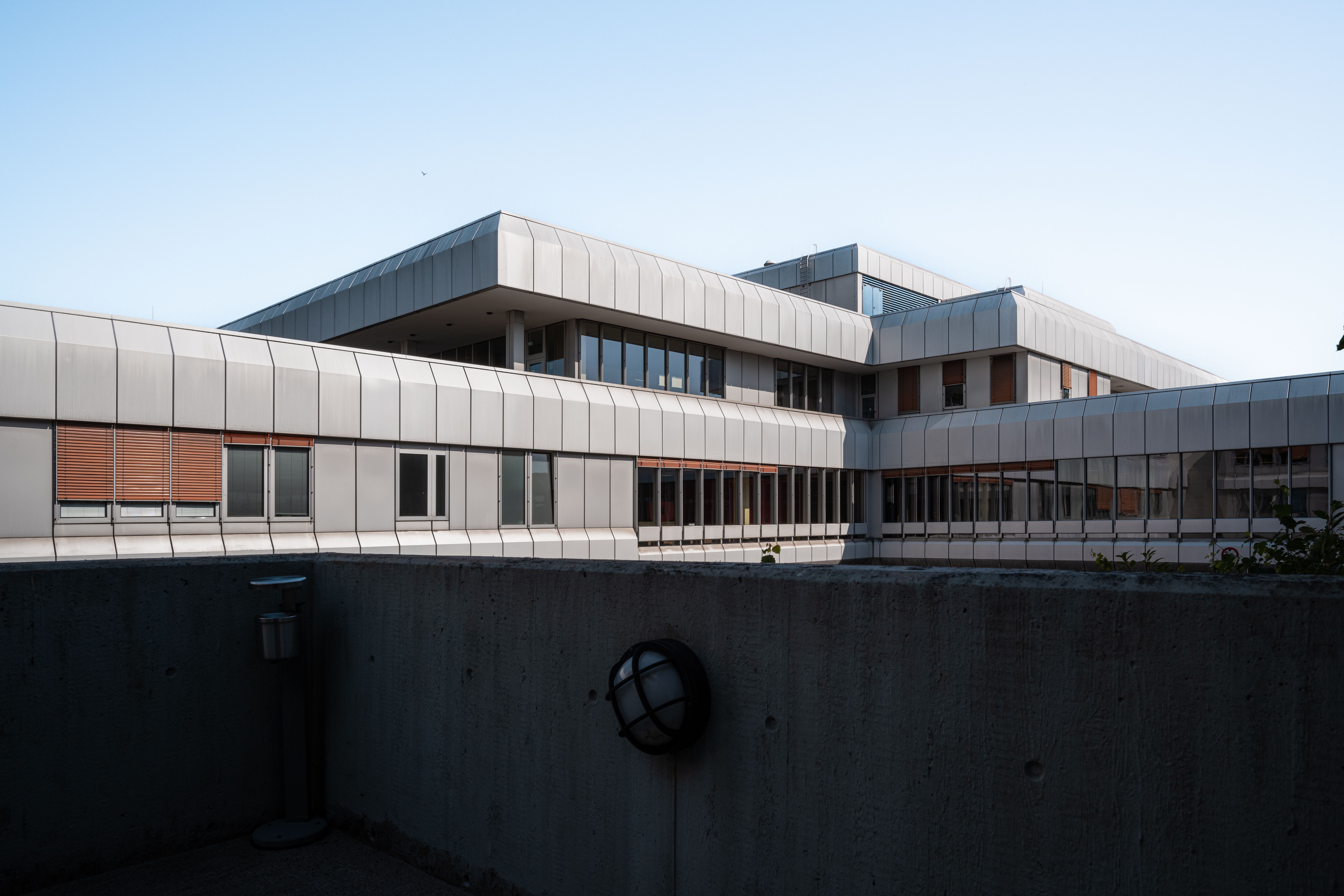 Angular view of a modern building with metallic facade and large windows, under a clear sky.